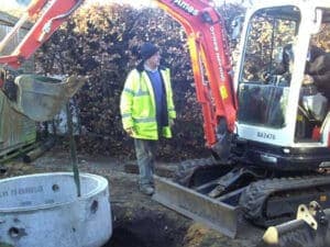 Excavator digging a drainage trench beside soakaway rings